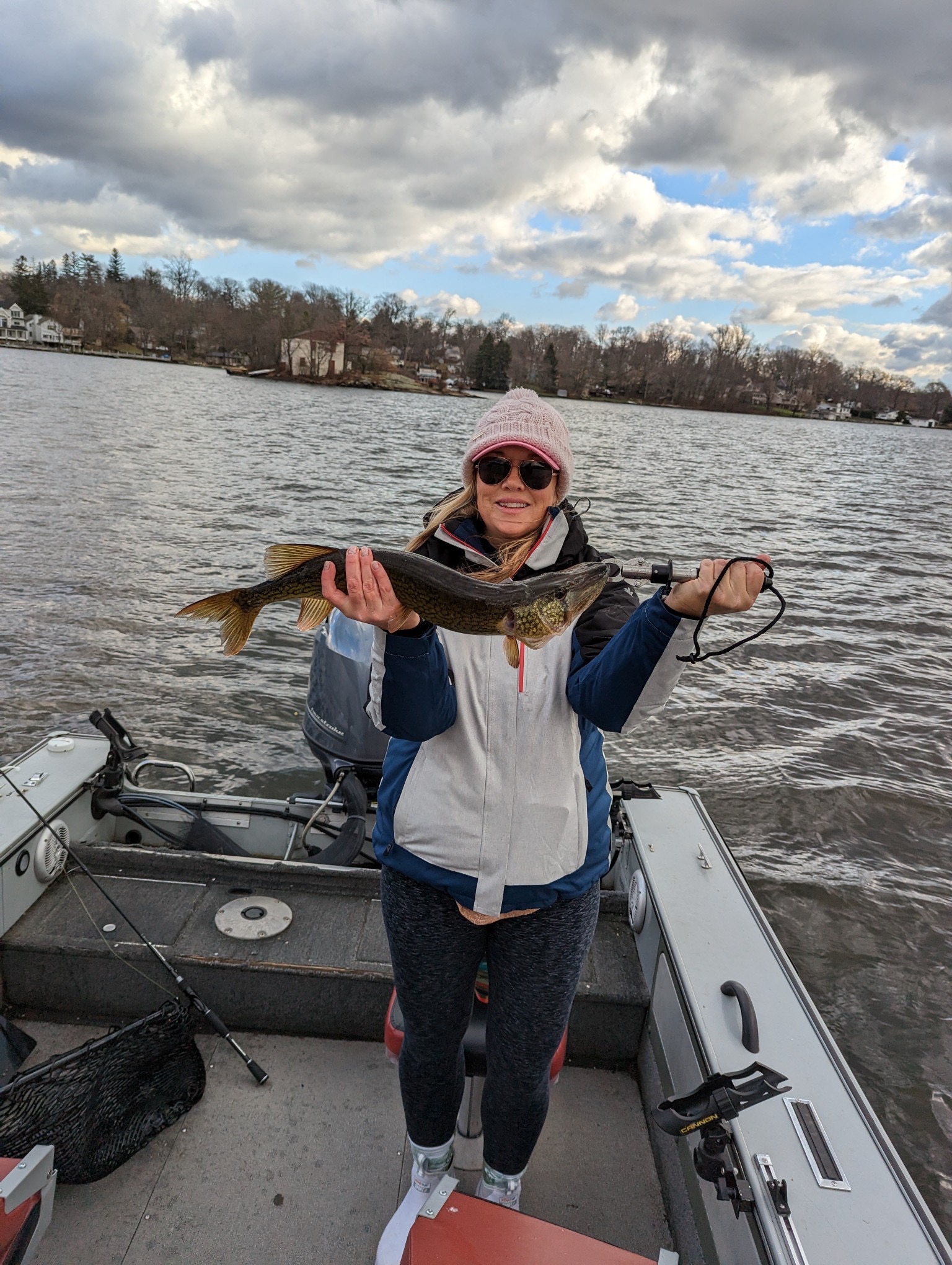Woman angler in winter gear holding large chain pickerel on lake