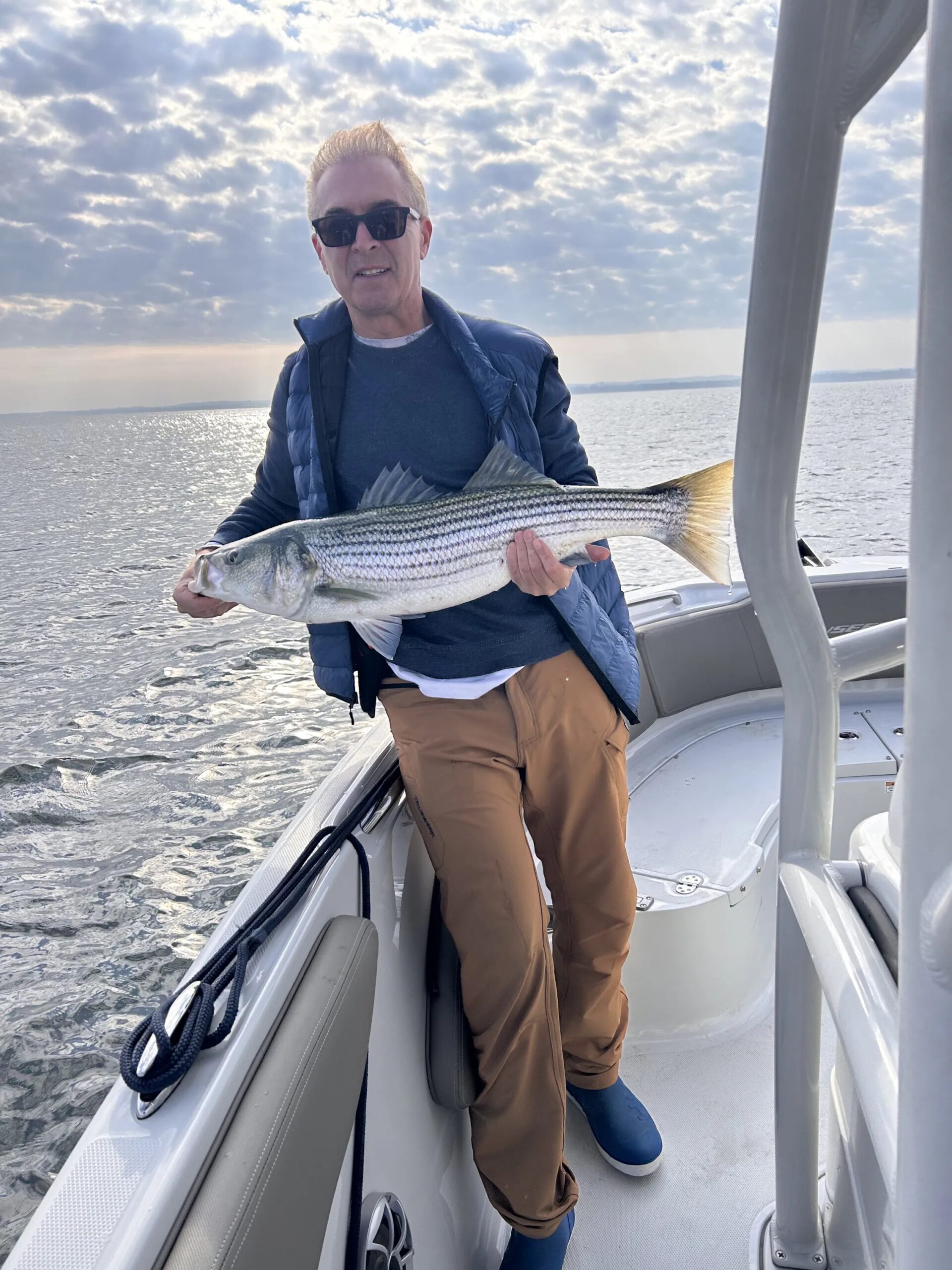 Angler holding large striped bass under mackerel-cloud sky on open water