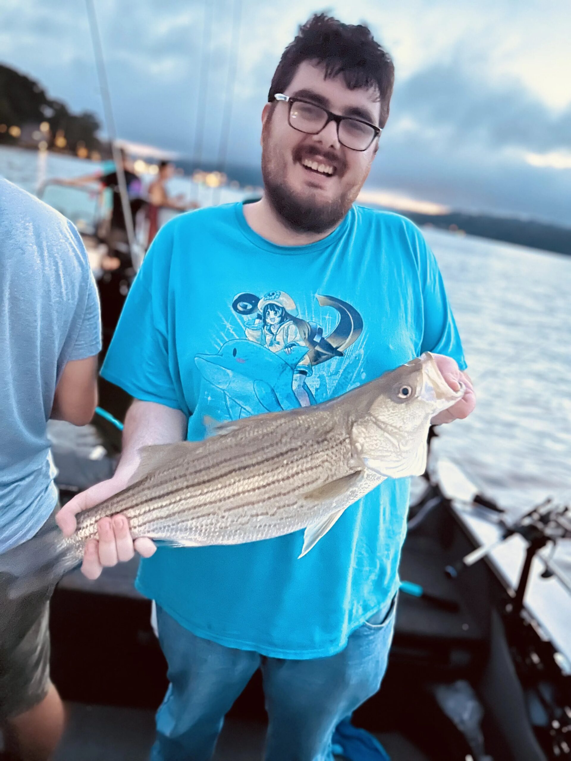 Young angler smiling with striped bass at dusk on the water
