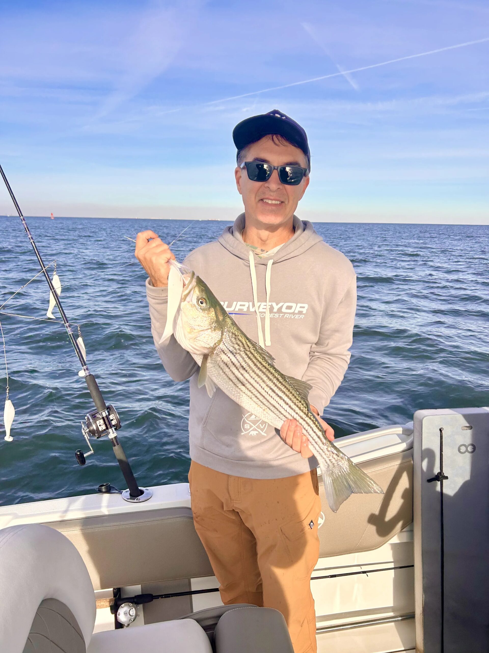Angler with striped bass aboard center-console fishing boat on open bay water